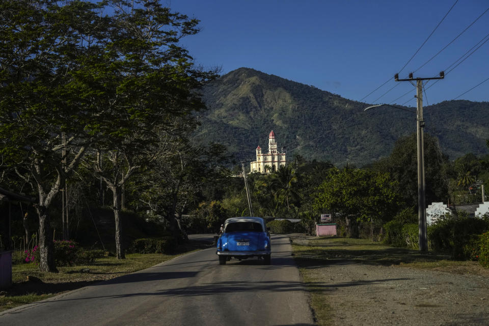 A classic American car heads down the road toward the shrine of the Virgin of Charity of El Cobre in El Cobre, Cuba, Sunday, Feb. 11, 2024. The Vatican-recognized Virgin, venerated by Catholics and followers of Afro-Cuban Santeria traditions, is at the heart of Cuban identity, uniting compatriots from the Communist-run Caribbean island to those who were exiled or emigrated to the U.S. (AP Photo/Ramon Espinosa)