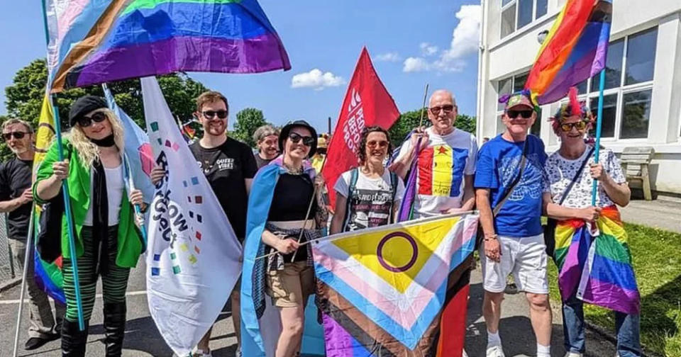 The image shows organisers of the 30th Foyle Pride attending Inishowen Pride earlier this year. It is a sunny day and they are all posing with Progressive Pride flags.