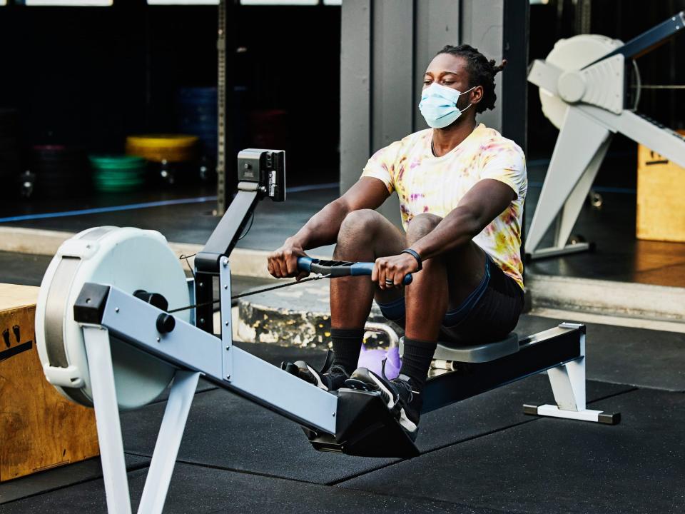 A man in a face mask on a rowing machine.