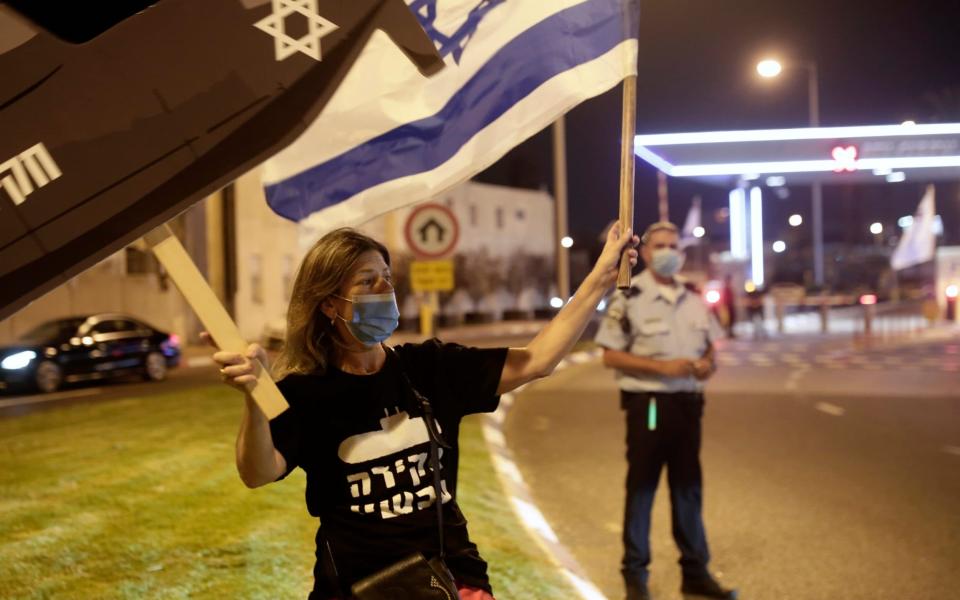 An anti-government protester waves an Israeli flag and a placard as a policeman watches a demonstration  - Maya Alleruzzo /AP