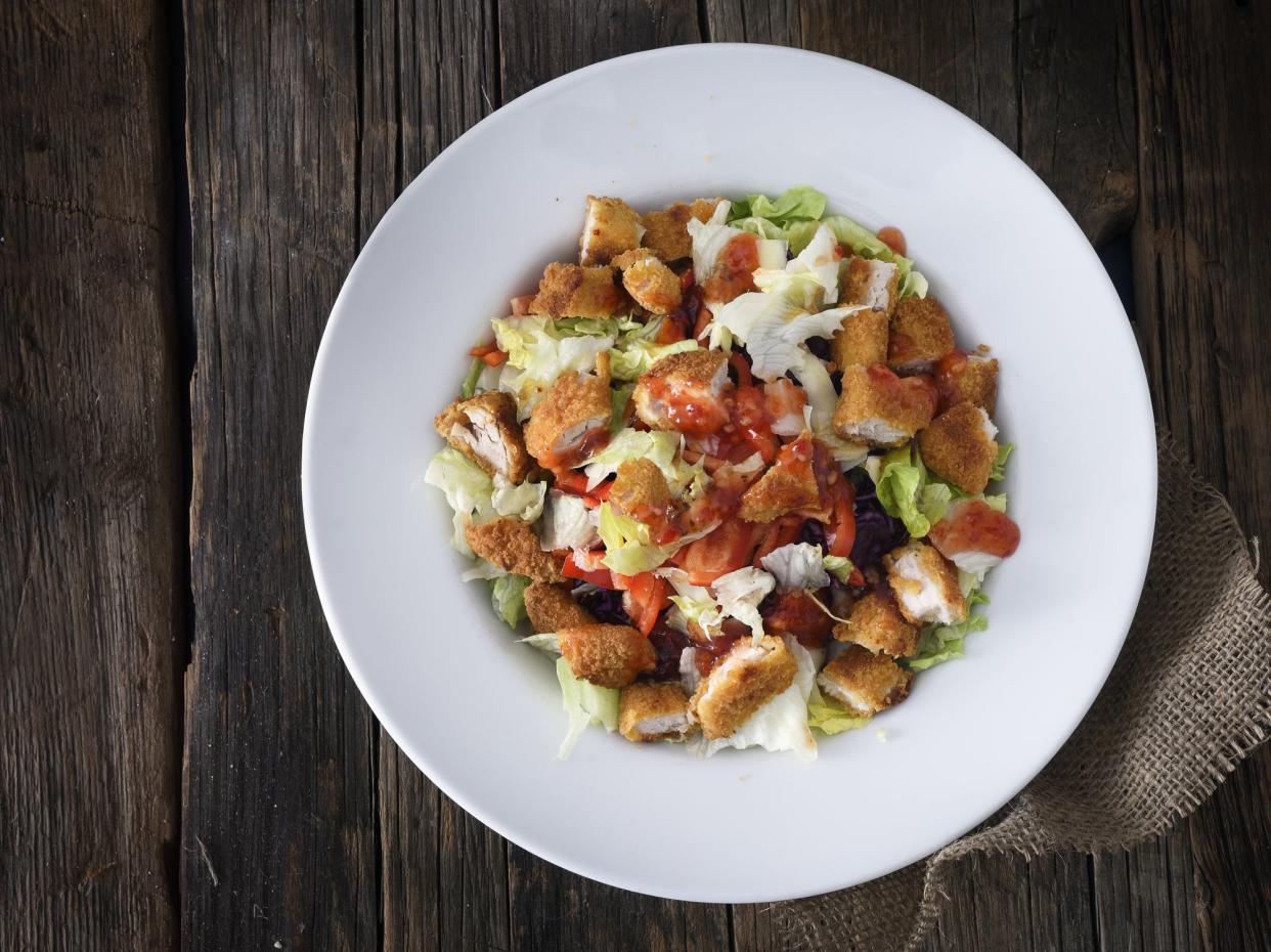 Crispy fried chicken salad with thai sauce, red bell pepper and red cabbage on a wooden background