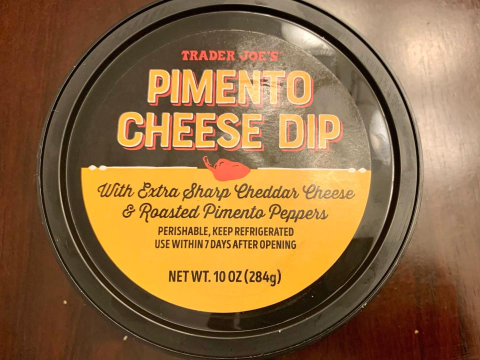 black and yellow tub of trader joe's pimento cheese dip on wood table