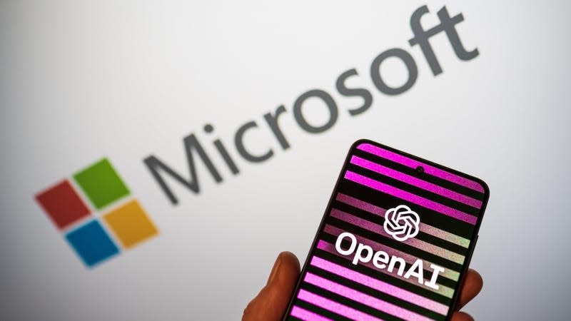 OpenAi's logo on a phone in front of Microsoft's logo in the background.