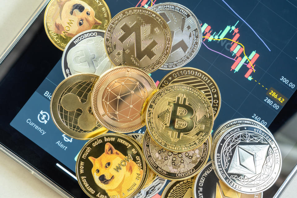 A range of different cryptocurrencies with a trading app displayed on a tablet in the background. (Source: Getty)