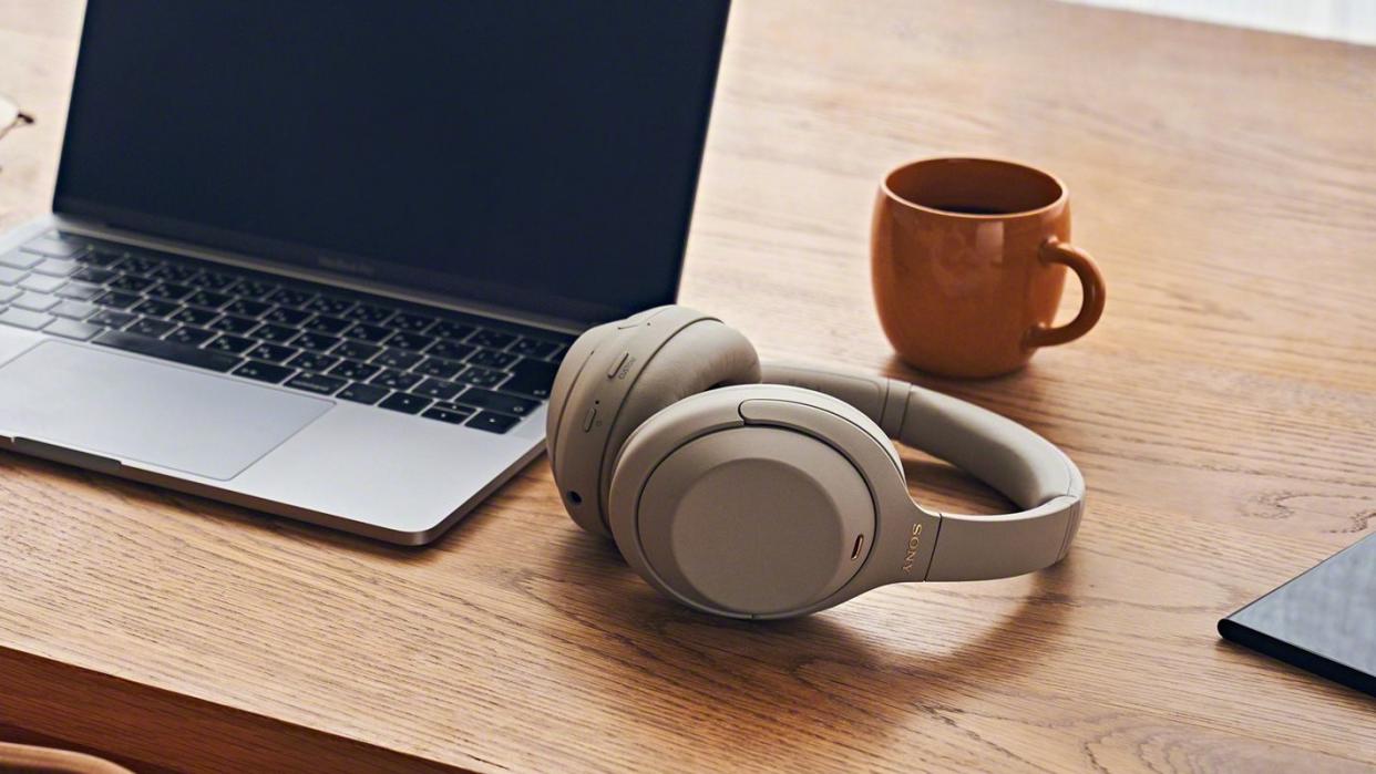  Beige Sony wireless headphones next to a laptop and mug. 