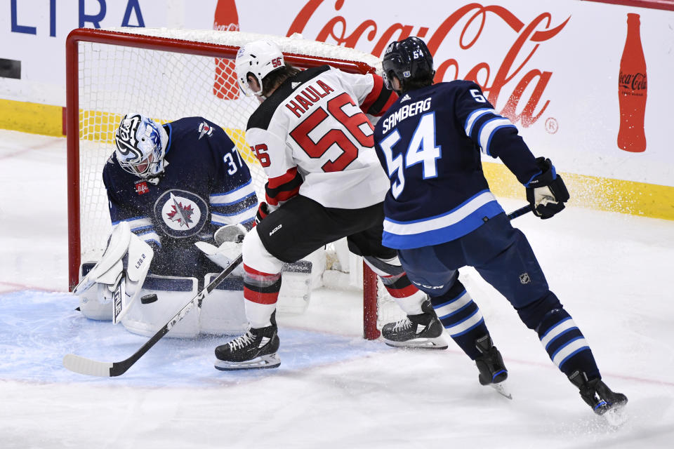 Winnipeg Jets goaltender Connor Hellebuyck (37) makes a save on New Jersey Devils' Erik Haula (56) as Jets' Dylan Samberg (54) defends during the third period of an NHL hockey game Tuesday, Nov. 14, 2023, in Winnipeg, Manitoba. (Fred Greenslade/The Canadian Press via AP)