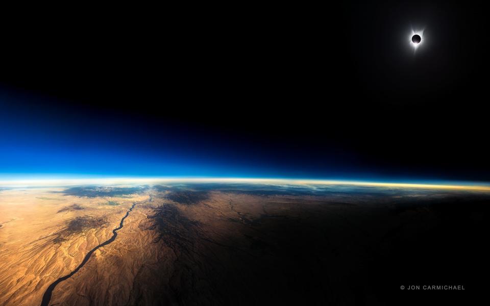 A total solar eclipse in the upper right of the photo with the moon's shadow cast down on the mountainous terrain below.