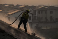 Firefighter Tylor Gilbert puts out hotspots while battling the Silverado Fire, Monday, Oct. 26, 2020, in Irvine, Calif. A fast-moving wildfire forced evacuation orders for 60,000 people in Southern California on Monday as powerful winds across the state prompted power to be cut to hundreds of thousands to prevent utility equipment from sparking new blazes. (AP Photo/Jae C. Hong)