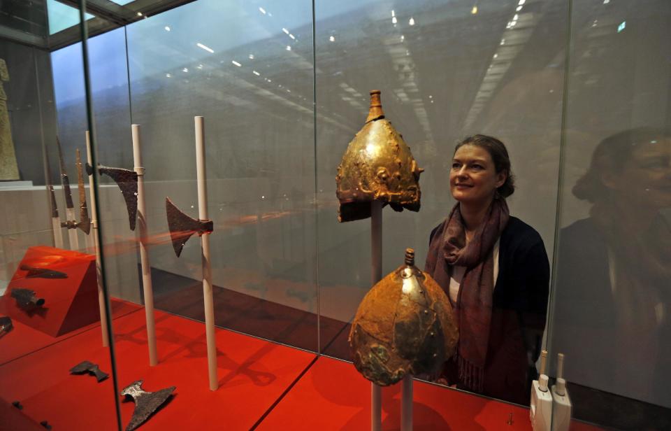 A British museum employee poses for the photographers behind a display of helmets at a new exhibition entitled 'Vikings: Life and Legend' at the British Museum in central London, Tuesday, March 4, 2014. The new exhibition strives to make people think again about the Scandinavian pillagers who raided and struck terror into English villages. The exhibition aims to show how Viking energy and ideas re-drew the map of the world, through the presentation of their ships, their weapons, their crafts, their words and even their skeletons. (AP Photo/Lefteris Pitarakis)