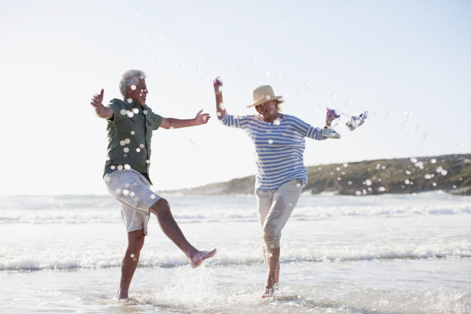 A senior couple splashes happily in the ocean on a beach.