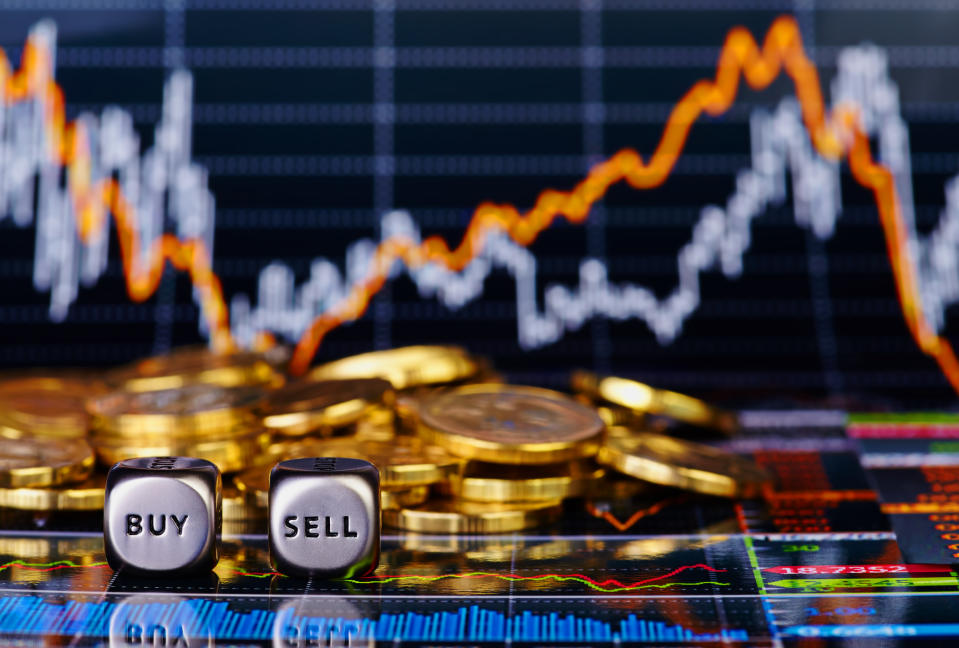 A pair of dice show buy and sell in front of a pile of gold coins and a financial chart.