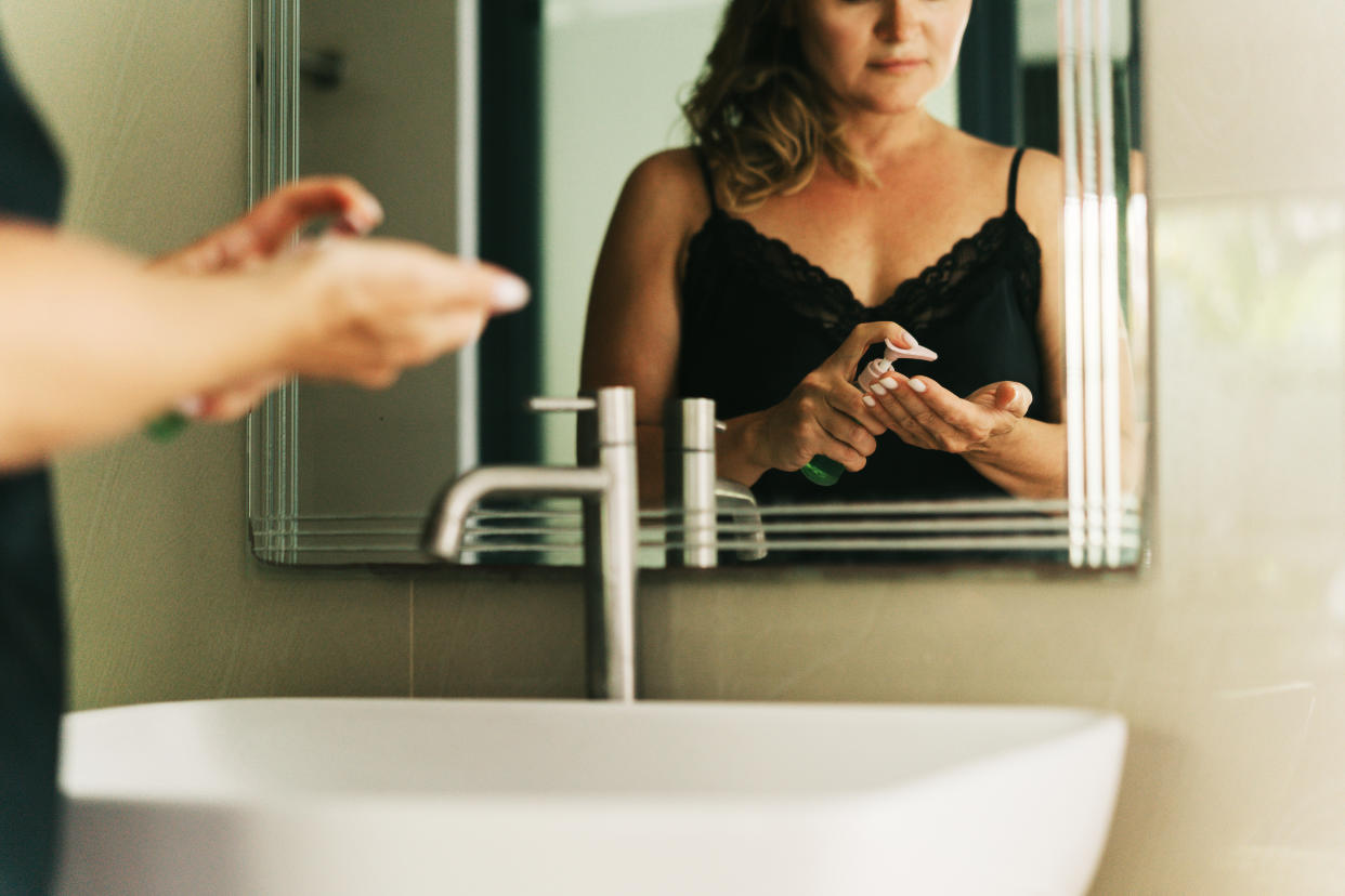 A beautiful middle-aged woman in a nightgown applies cosmetics in the bathroom near the mirror. Daily morning routine, facial skin care, home treatment. A room in a luxury hotel, business trip or vacation in a high class apartment. Relaxation, mindfulness and zen-like