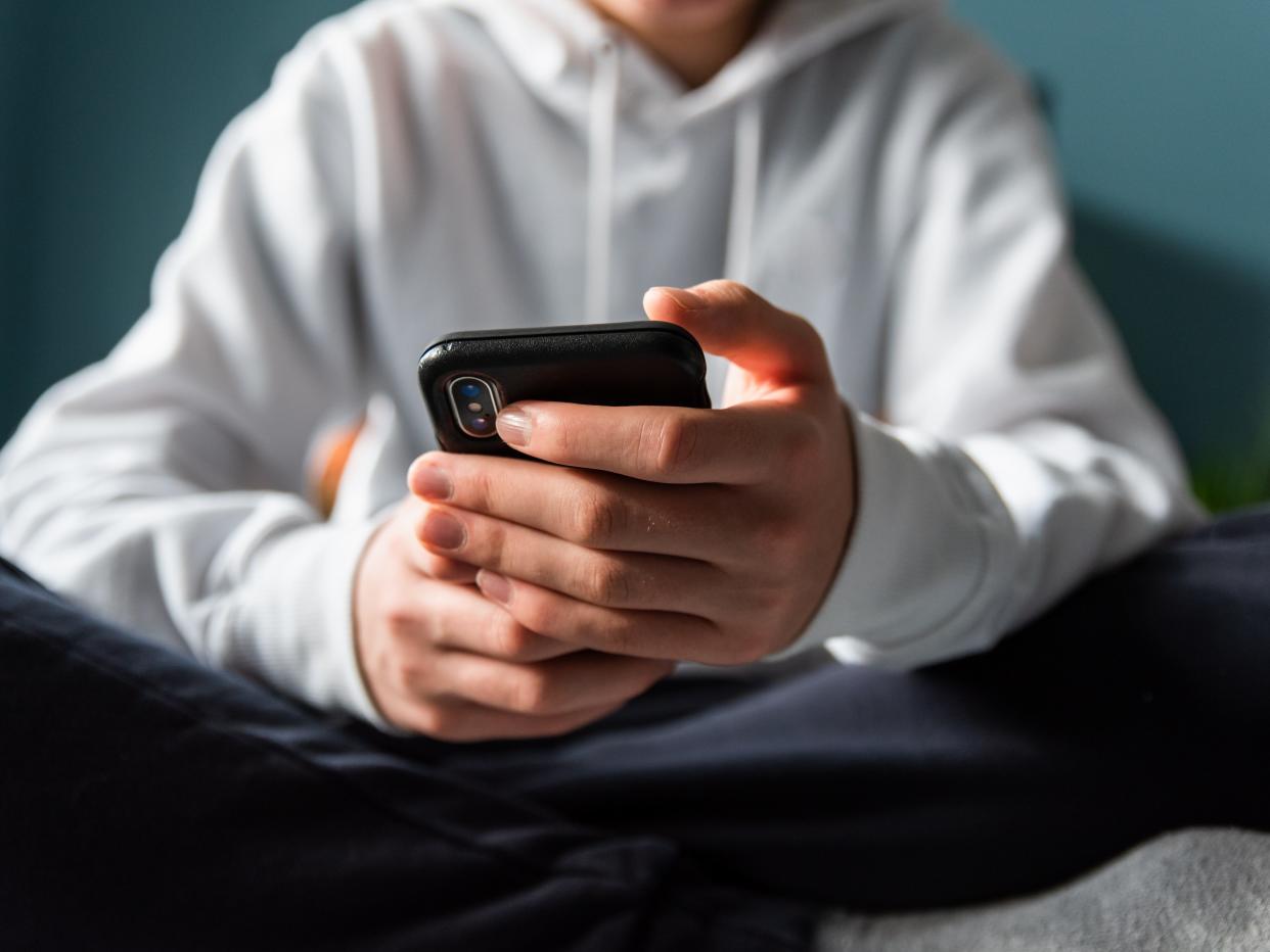 Close up of hands of teen boy in white sweater texting on phone