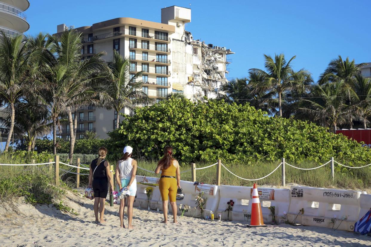 Daniela Valido, left, Daphnie Lucero, center, and Rebeca Salazal, right, stop at a makeshift memorial near the site of the partially collapsed South Florida condo building, Champlain Towers South, in Surfside, Fla., Sunday, July 4, 2021.