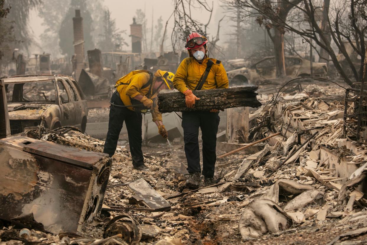 Jackson County District 5 firefighter Captain Aaron Bustard, right, and Andy Buckingham work on a smouldering fire in a burned neighbourhood as destructive wildfires devastate the region on Friday (AP)