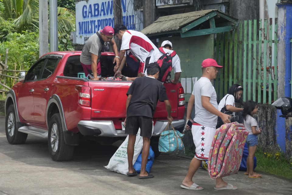 Evacuees carry their belongings as they arrive at a temporary relocation site at a school in Daraga town, Legaspi, Albay province, northeastern Philippines, Saturday, June 10, 2023. Monsoon rains that could be unleashed by an offshore typhoon were complicating worries of villagers threatened by restive Mayon volcano that has forced thousands of people to flee from their homes.(AP Photo/Aaron Favila)