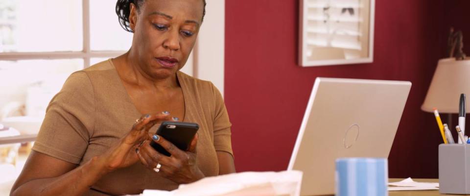 An older black woman uses her phone and laptop to do her taxes