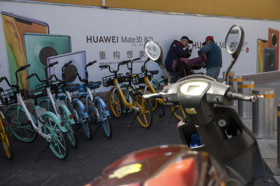 In this photo taken Sunday, March 22, 2020, men chat near advertisements for Huawei mobile phones in Beijing. Chinese tech giant Huawei says Tuesday, March 31, 2020, its 2019 sales rose 19.1% over a year earlier despite U.S. sanctions that hampered its smartphone and network equipment businesses. The company is embroiled in a series of disputes with Washington, which says Huawei is a security risk, an accusation it denies. (AP Photo/Ng Han Guan)