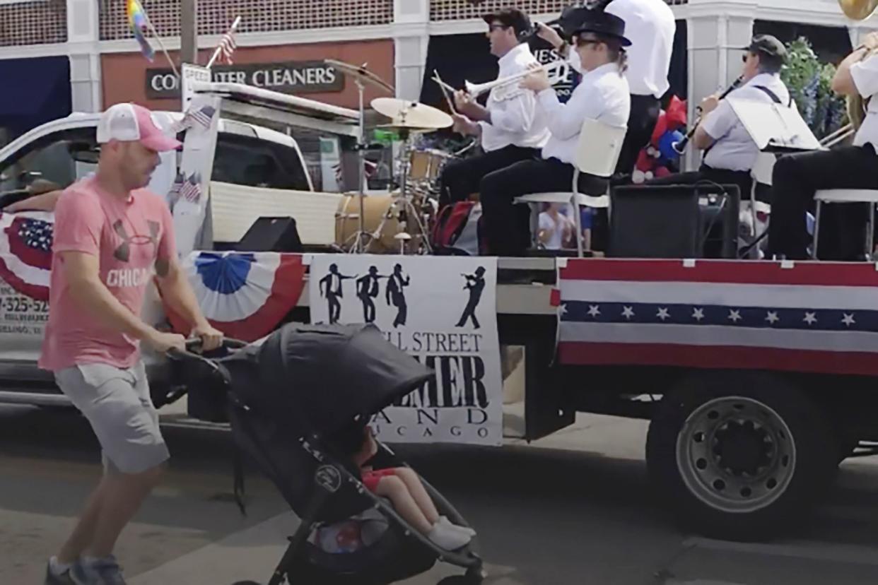 In this still image from video, a man runs for cover with a child in a stroller after gunfire was heard at the Fourth of July parade in the Chicago suburb of Highland Park, Monday morning, July 4, 2022.