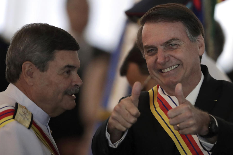 In this March 28, 2019 photo, Brazil's President Jair Bolsonaro flashes two thumbs up standing next to Adm. Marcus Vinicius Oliveira dos Santos, Supreme Military Court president, who presented Bolsonaro with the Order of Military Judicial Merit, in Brasilia, Brazil. Bolsonaro, a former army captain who waxes nostalgic for the 1964-1985 dictatorship, on Monday asked Brazil's Defense Ministry to organize "due commemorations" to mark the upcoming March 31st anniversary of Brazil's 1964 military coup. (AP Photo/Eraldo Peres)
