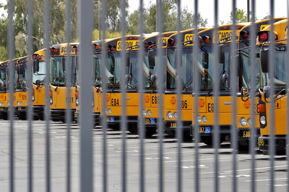 Dormant school buses are secured at a facility Friday, April 17, 2020, in Tempe, Ariz. Cities across Arizona are tightening their belts and revising previously rosy budget forecasts as they begin to feel the financial impact of the coronavirus outbreak now shutting down much of the economy across the state. (AP Photo/Matt York)