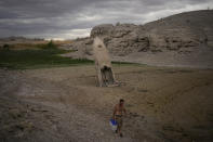 A man walks by a formerly sunken boat standing upright into the air with its stern buried in the mud along the shoreline of Lake Mead at the Lake Mead National Recreation Area near Boulder City, Nev., June 22, 2022. Las Vegas and Phoenix may be forced to ration water or restrict growth. Farmers may confront painful decisions about which crops to stop planting. Those are a few of the dire consequences that could result if states, cities and farms cannot agree on how to cut the amount of water they draw from the Colorado River. (AP Photo/John Locher)