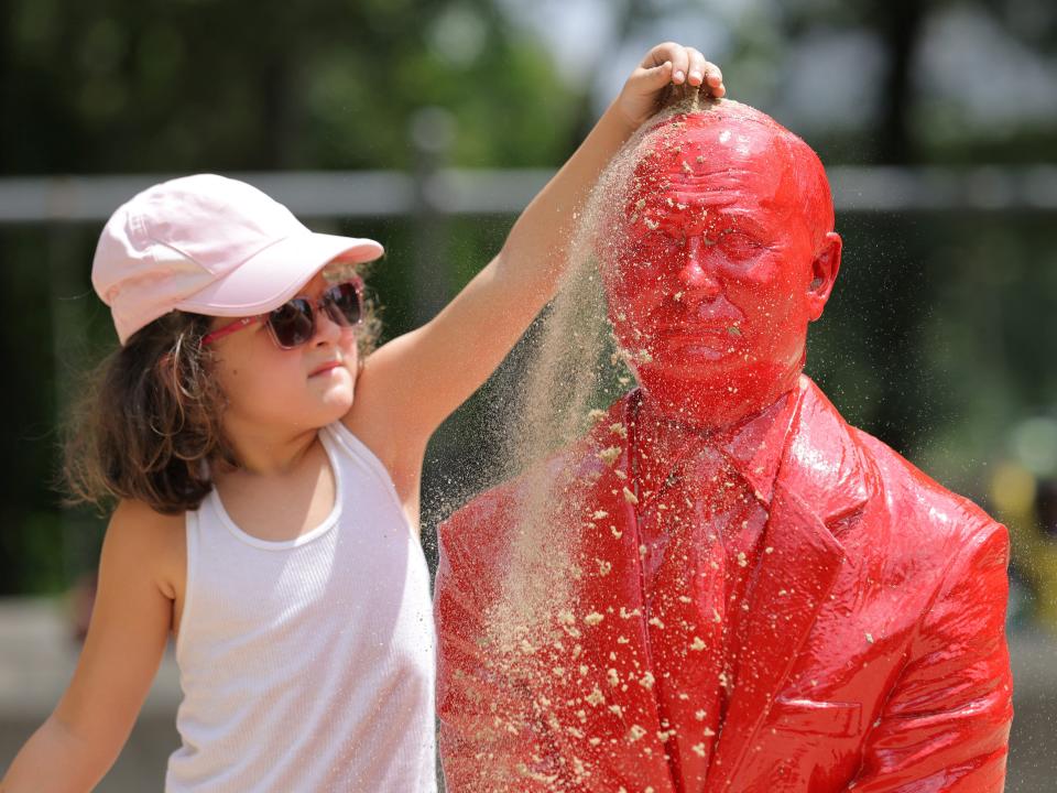 A child pours sand on a statue of Russian President Vladimir Putin riding a tank created by French artist James Colomina in Central Park in Manhattan, New York City, U.S., August 2, 2022.
