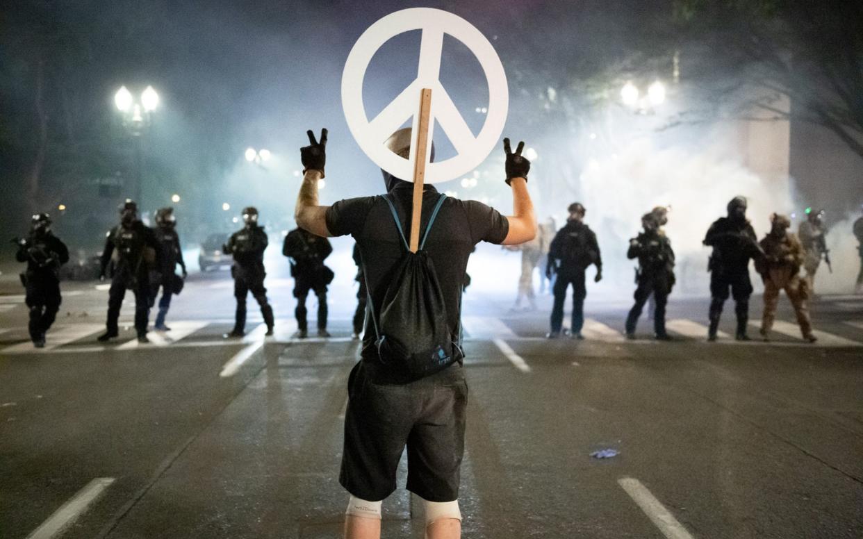 A protester holds up two peace signs in front of a wall of Department for Homeland Security officers and local police in Portland, Oregon - Mark McKenna