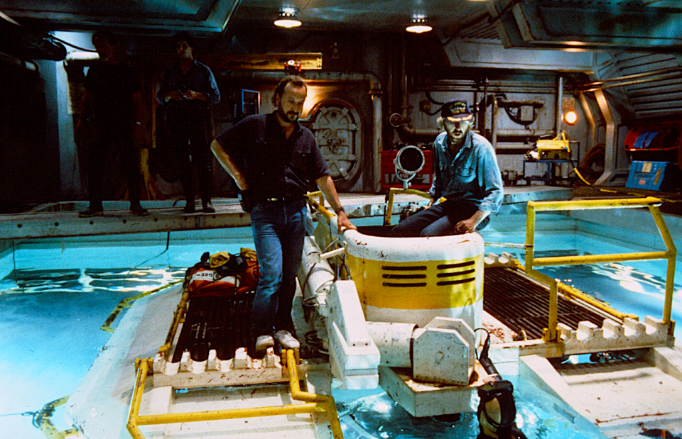 two men in jeans stand on top of diving equipment in a pool