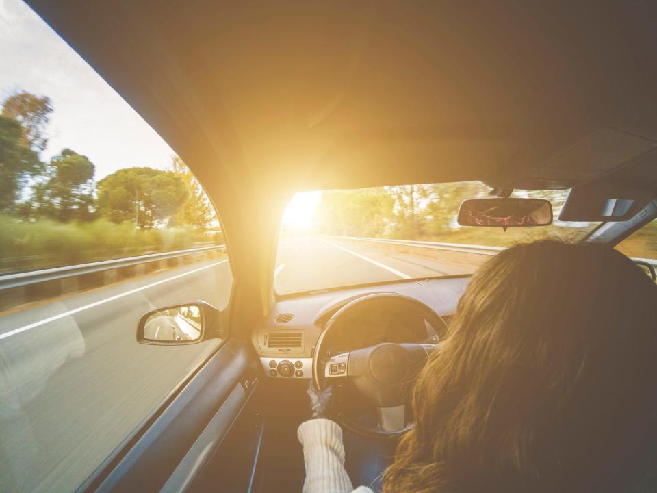 Woman driving a car on a highway towards the sunset