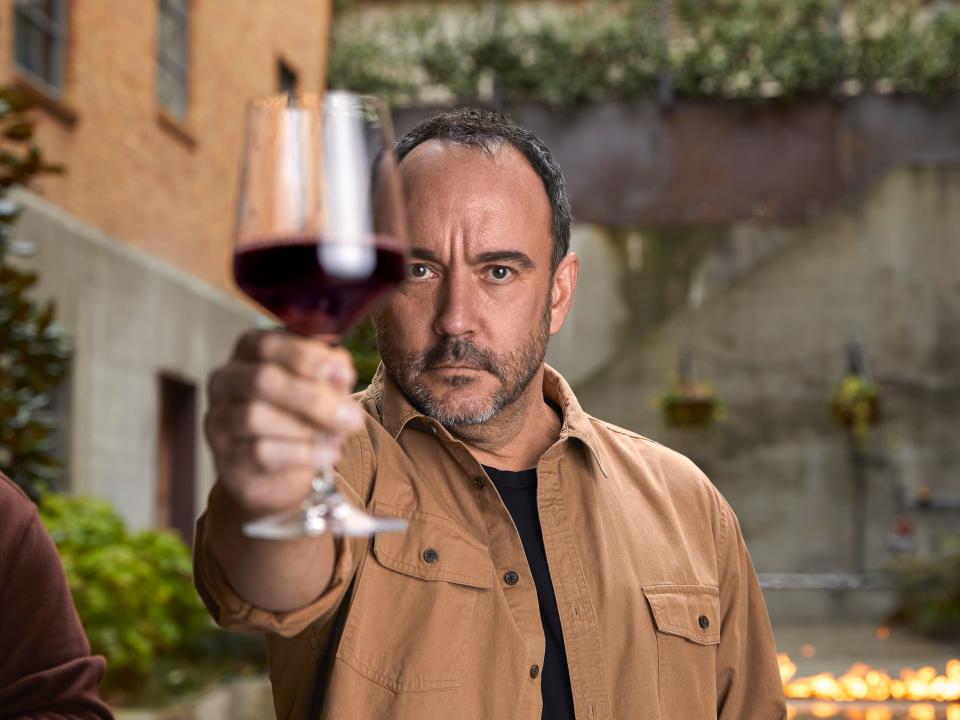 Dave Matthews holding a glass of wine in front of his face