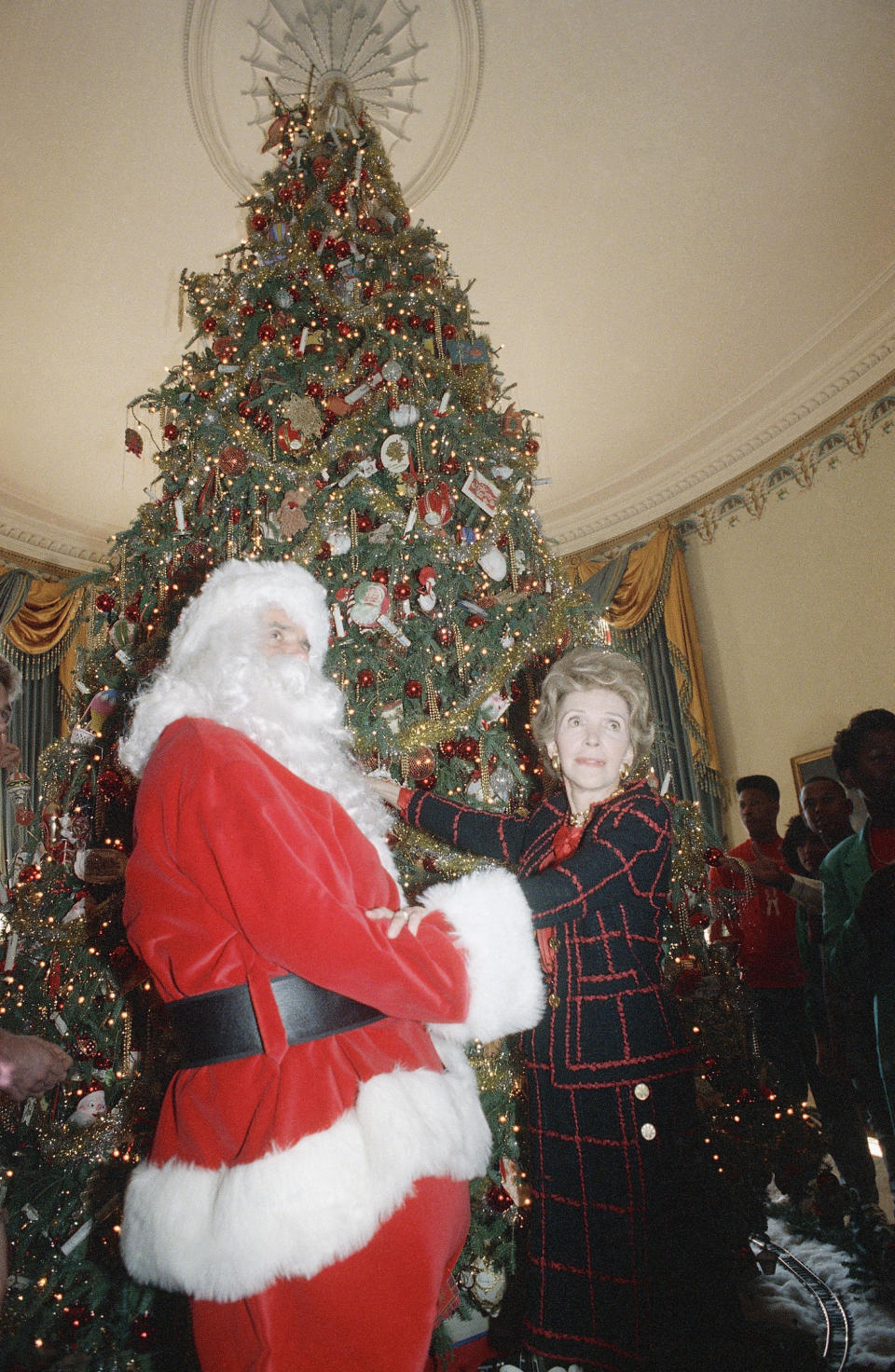 First lady Nancy Reagan with the help of comedian Rich Little, dressed as Santa Clause, takes part in the press preview of the White House Christmas decorations on Monday, Dec. 12, 1988 in Washington. This will be the last Christmas of the Reagan era. (AP Photo/Barry Thumma)
