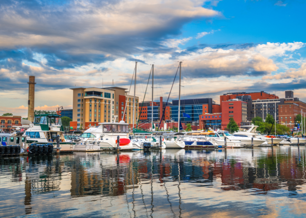 A harbor with boats docked in front of a city skyline of modern and older buildings with brick facades.