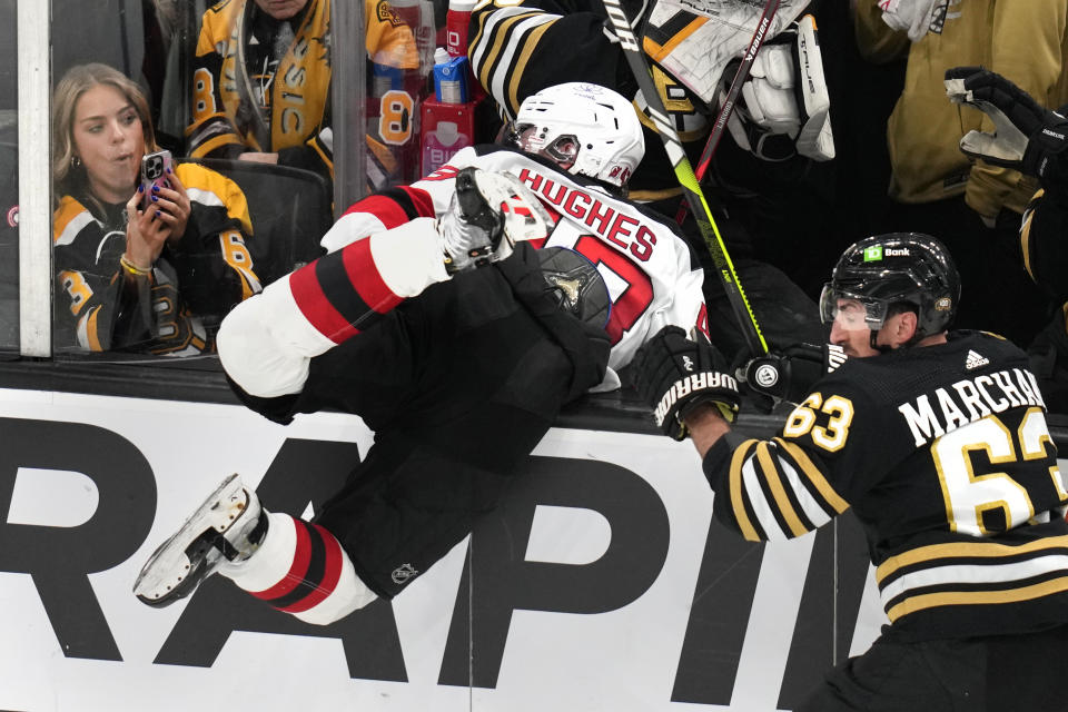 New Jersey Devils defenseman Luke Hughes (43) is launched into the bench by Boston Bruins left wing Brad Marchand (63) during the second period of an NHL hockey game, Monday, Jan. 15, 2024, in Boston. (AP Photo/Charles Krupa)