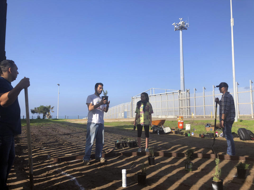 CORRECTS LAST NAME TO WATMAN INSTEAD OF WALTMAN Daniel Watman, second from left, who oversees a cross-border garden in San Diego, Calif., and Tijuana, Mexico, speaks with volunteers as he holds the first plant to be put in the ground after the Border Patrol bulldozed the patch earlier this month in Friendship Park, located within California's Border Field State Park on Saturday, Jan. 25, 2020. The U.S. Border Patrol, reacting to a breach it discovered in a steel-pole border wall believed to be used by smugglers, gave activists no warning this month when it bulldozed the U.S. side of a cross-border garden on an iconic bluff overlooking the Pacific Ocean. On Saturday, after a public apology for "the unintentional destruction," the agency allowed the activists in a highly restricted area to resurrect the garden. (AP Photo/Elliot Spagat)