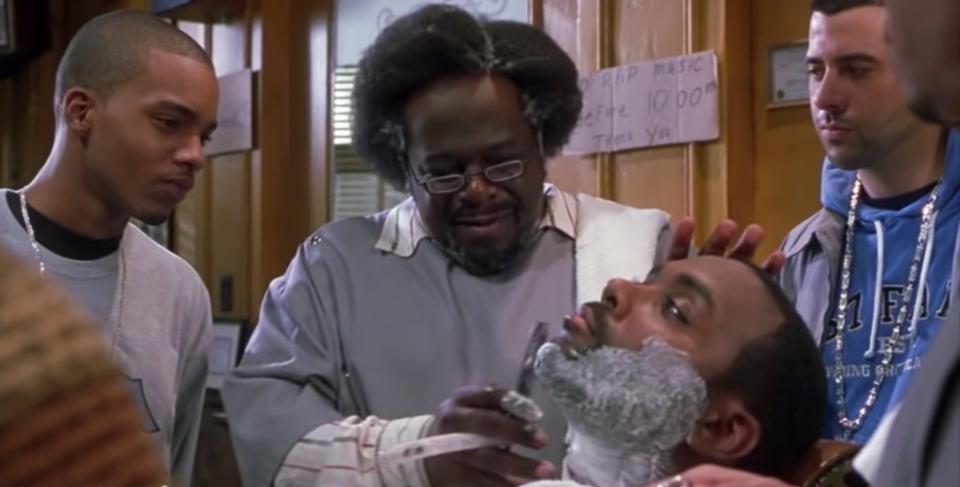 Characters from the movie "Barbershop" are watching as Cedric the Entertainer, who plays Eddie, is shaving a customer