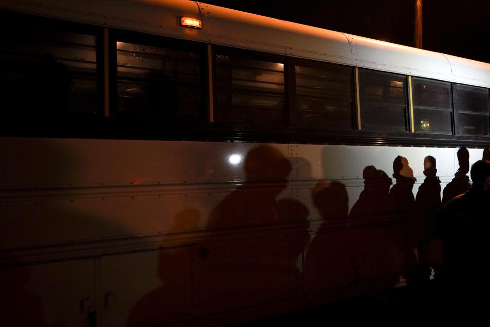 In this May 11, 2021, file photo shadows of migrants lined up at an intake area are cast along the side of a bus after turning themselves in upon crossing the U.S.-Mexico border in Roma, Texas. (AP Photo/Gregory Bull, File)