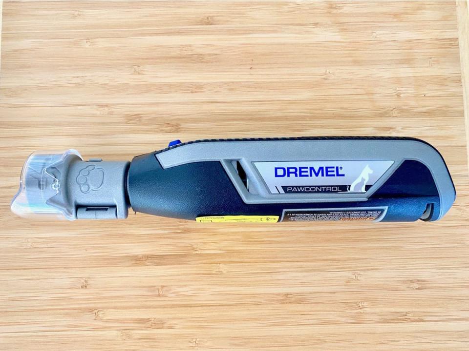 The black and gray Dremel 7760 PawControl Cordless Pet Nail Grinder sits on a wooden surface.