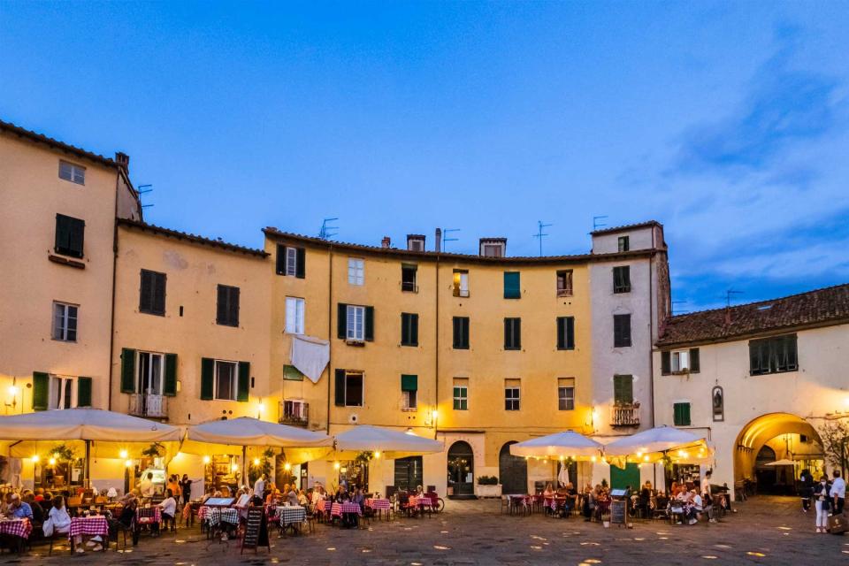 Tourists sitting at the outdoor tables in Piazza dell'Anfiteatro of Lucca, an elliptical shape square surrounded by a ring of buildings that follows the former second century Roman amphitheater of the city.