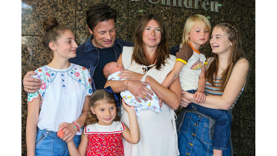 Jamie Oliver and Jools Oliver and children posing with youngest child outside Portland Hospital