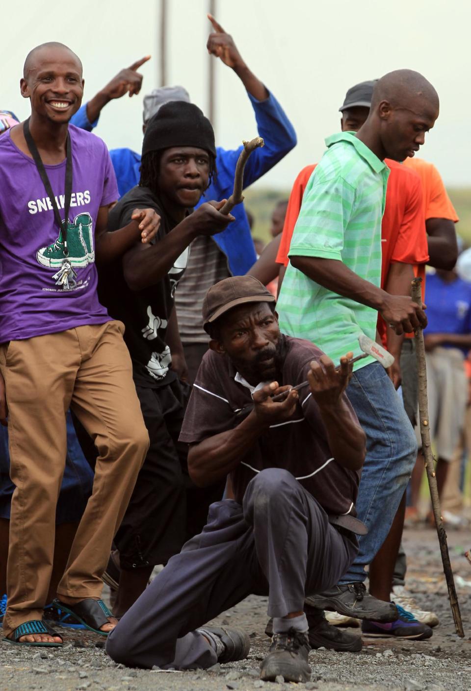 Residents sing as a man holds a golf club like a gun and aims it at police officers during a protest at Zithobile in Bronkhorstspruit, near Pretoria, South Africa, Thursday, Feb. 6, 2014. Demonstrators set several buildings, including a clinic, on fire on Wednesday in the Bronkhorstspruit district, east of the capital, Pretoria, to protest what they say are high electricity prices. (AP Photo/Themba Hadebe)