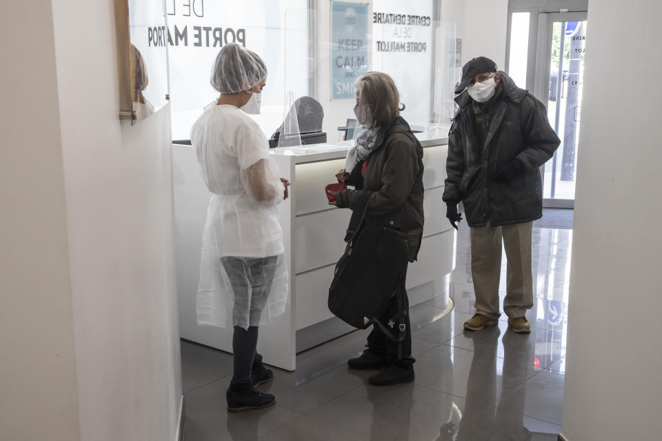 In this Wednesday, May 13, 2020 photo, dentist Sabrine Jendoubi, left, speaks to an unidentified patient upon her arrival at a dental office in Paris. Those with toothache that suffered through France's two-month lockdown, finally have hope to end the pain. Dental practices are cautiously re-opening and non-emergency dentist appointments are now permitted around the country, as the French government eased confinement restrictions from Monday. (AP Photo/Michel Euler)