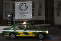 A taxi passes a large banner promoting the Tokyo 2020 Olympics in Tokyo, Tuesday, March 24, 2020. IOC President Thomas Bach has agreed "100%" to a proposal of postponing the Tokyo Olympics for about one year until 2021 because of the coronavirus outbreak, Japanese Prime Minister Shinzo Abe said Tuesday. (AP Photo/Jae C. Hong)