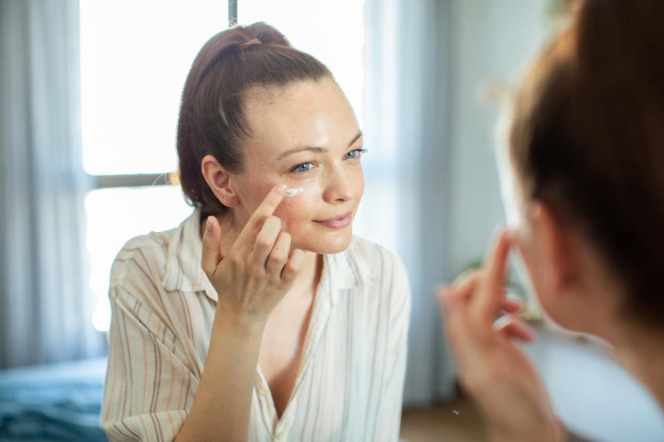 woman putting moisturizer on in mirror