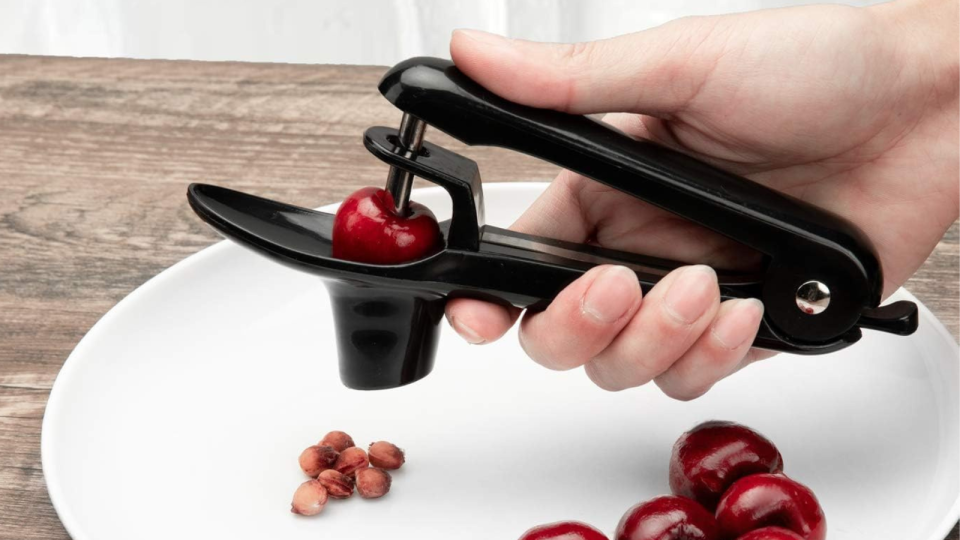 hand using a black cherry pitter to pit cherries