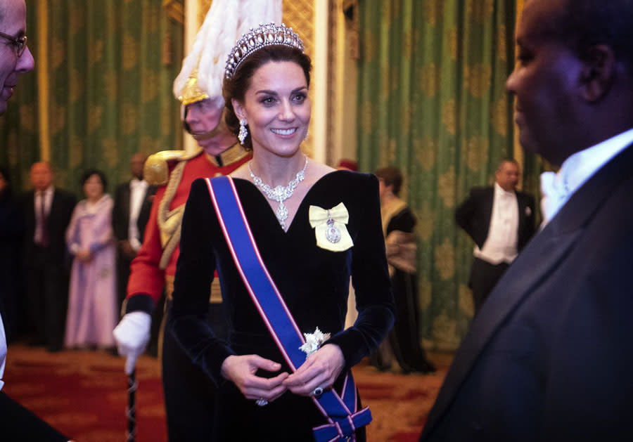 Une stature de princesse. Si Kate Middleton n’en a pas encore le titre, elle en a déjà l’allure. Robes incroyables, diadèmes… L’épouse du prince William ressemble à un personnage de contes de fées. Mercredi soir encore, elle l’a prouvé lors d’une grande réception au palais de Buckingham. La reine recevait le corps diplomatique international basé à Londres, et pour l’occasion, plusieurs membres de la famille royale étaient de la partie, dont le prince William et Camilla, duchesse de Cornouailles.Kate Middleton était incontestablement la star de la soirée, et des mille invités, on ne voyait qu’elle. La duchesse de Cambridge avait opté pour une longue robe noire en velours signée Alexander McQueen, maison chère à son coeur puisqu'elle a conçu sa robe de mariée. Une tenue surprenante avec une couleur sombre dans laquelle on la voit peu. Sur sa tête, Kate Middleton portait The Lovers Knot, une tiare connue du public puisqu’elle a été commandée par la reine Mary en 1914 et Kate l’a déjà portée à plusieurs reprises. Mais c’est surtout la princesse Diana qui a rendu cette couronne célèbre puisqu’elle était sa favorite. Kate Middleton en a aussi fait sa pièce phare puisqu’elle l’a portée à six reprises depuis 2013. Pour compléter cette parure, la duchesse avait opté pour le collier Nizam of Hyderabad qu’elle avait déjà porté en 2014 à la National Portrait Gallery. Un collier composé de treize émeraudes et de diamants signé Cartier, qui a appartenu à la reine d’Angleterre et qu’elle a offert à Kate Middleton comme cadeau de mariage. Enfin, Kate Middleton portait à son sein un badge jaune avec un médaillon sur lequel se trouve un portrait d’Elisabeth II, signifiant son appartenance à l’Ordre royal victorien, une distinction offerte par la reine.