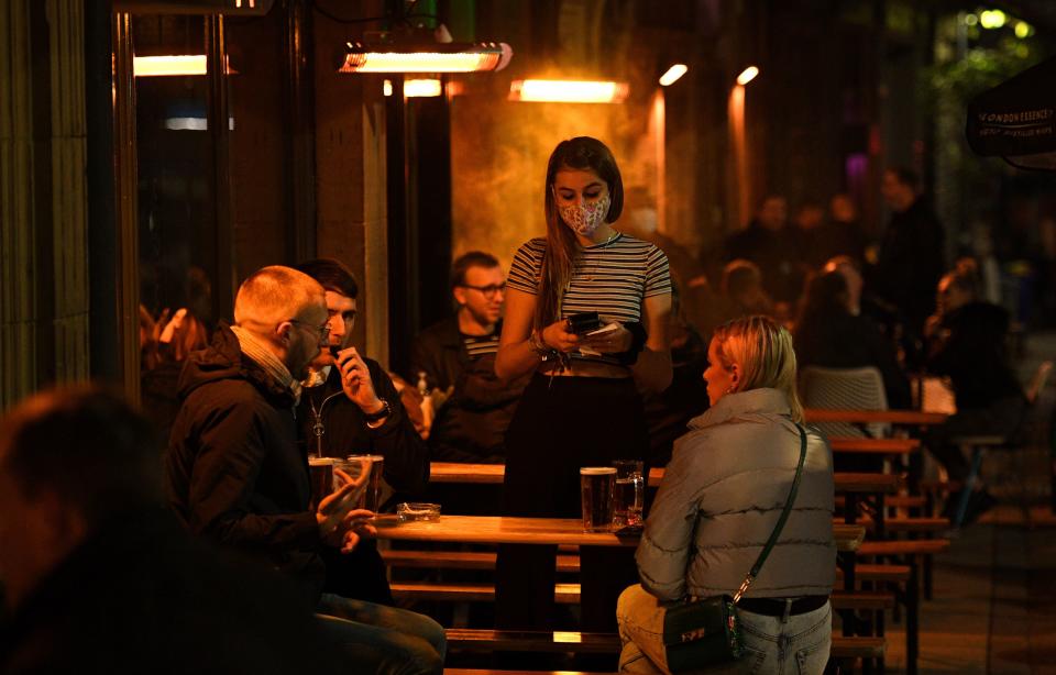 A waitress wearing a face mask or covering due to the COVID-19 pandemic, takes customers' orders as they sit outside a bar in Leeds, northern England on November 4, 2020, on the eve of a second novel coronavirus COVID-19 lockdown in an effort to combat soaring infections. - English pubs call last orders at the bar for a month on Wednesday evening, as the country effectively shuts down from November 5, for the second time this year to try to cut coronavirus cases. Prime Minister Boris Johnson insisted that the lockdown for England would end 