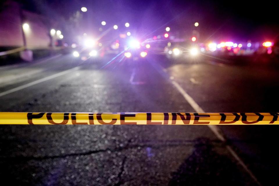 Yellow police tape across a street with police vehicles in the background