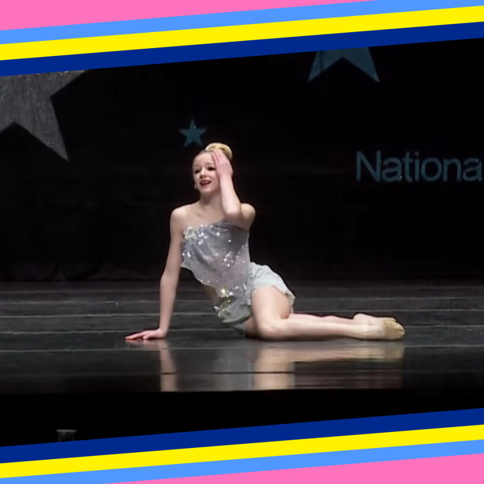 Dancer in a sparkling costume performs on stage, hand by face in a dramatic gesture