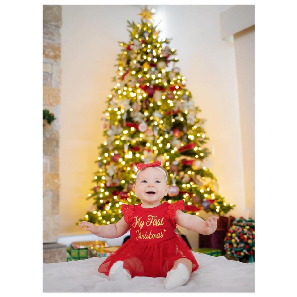 Bindi Irwin's daughter, Grace Warrior Irwin Powell wears a red dress and sits in front of a Christmas tree. Photo: Instagram/robertirwinphotography.